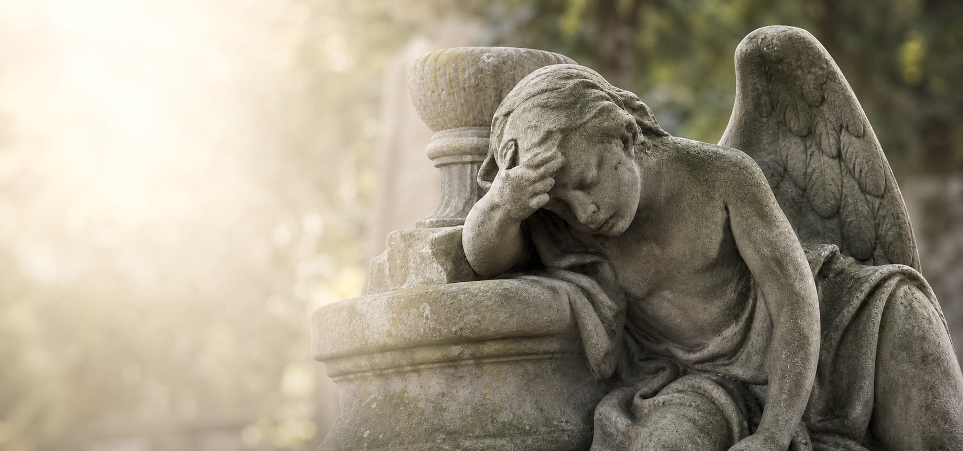 Trauernder Steinengel an einem Grabmal, umgeben von weichem Licht